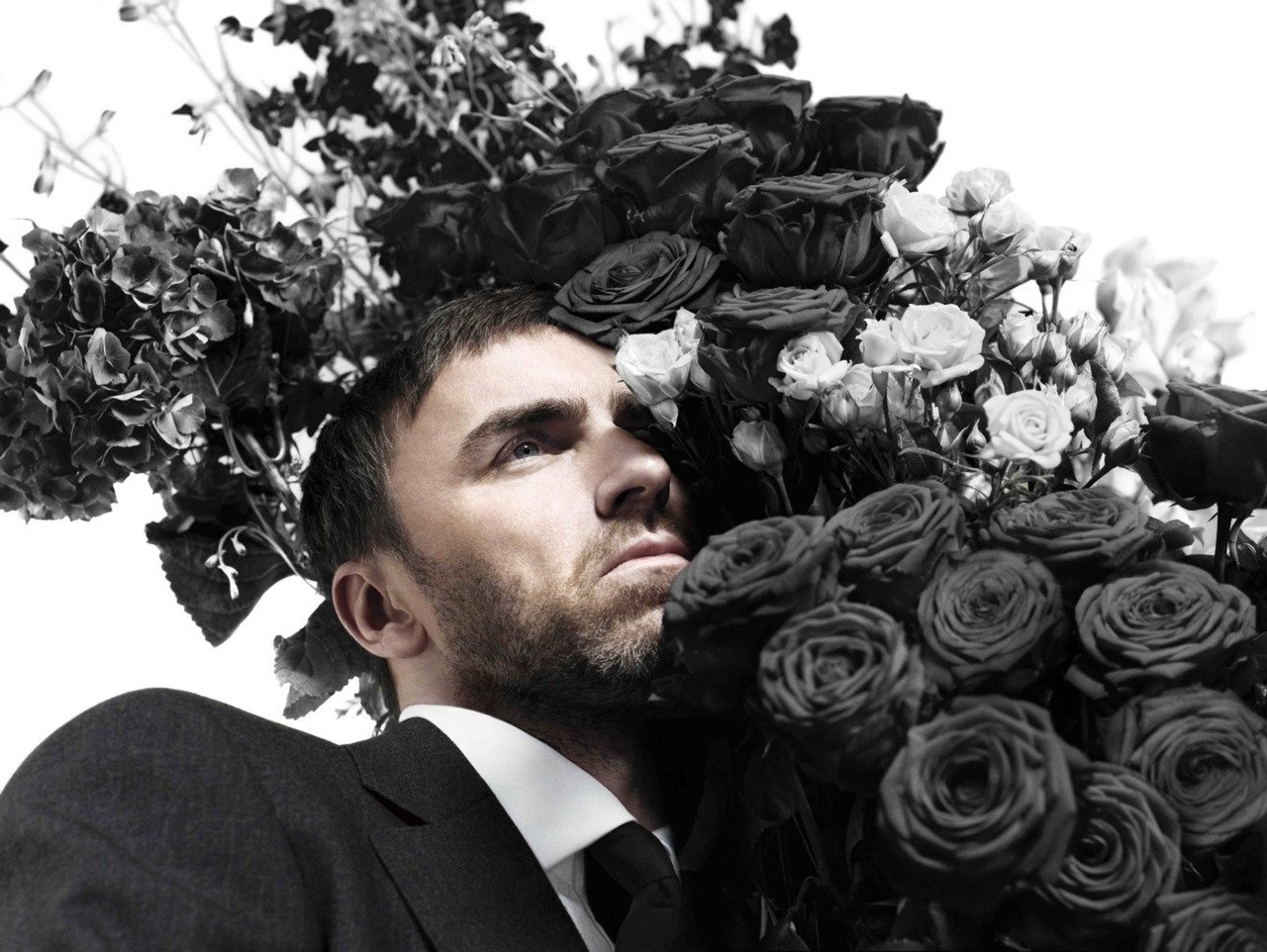 raf simons in a suit next to black roses