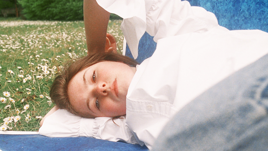 A person lies on a blanket in a field of flowers looking down towards the camera