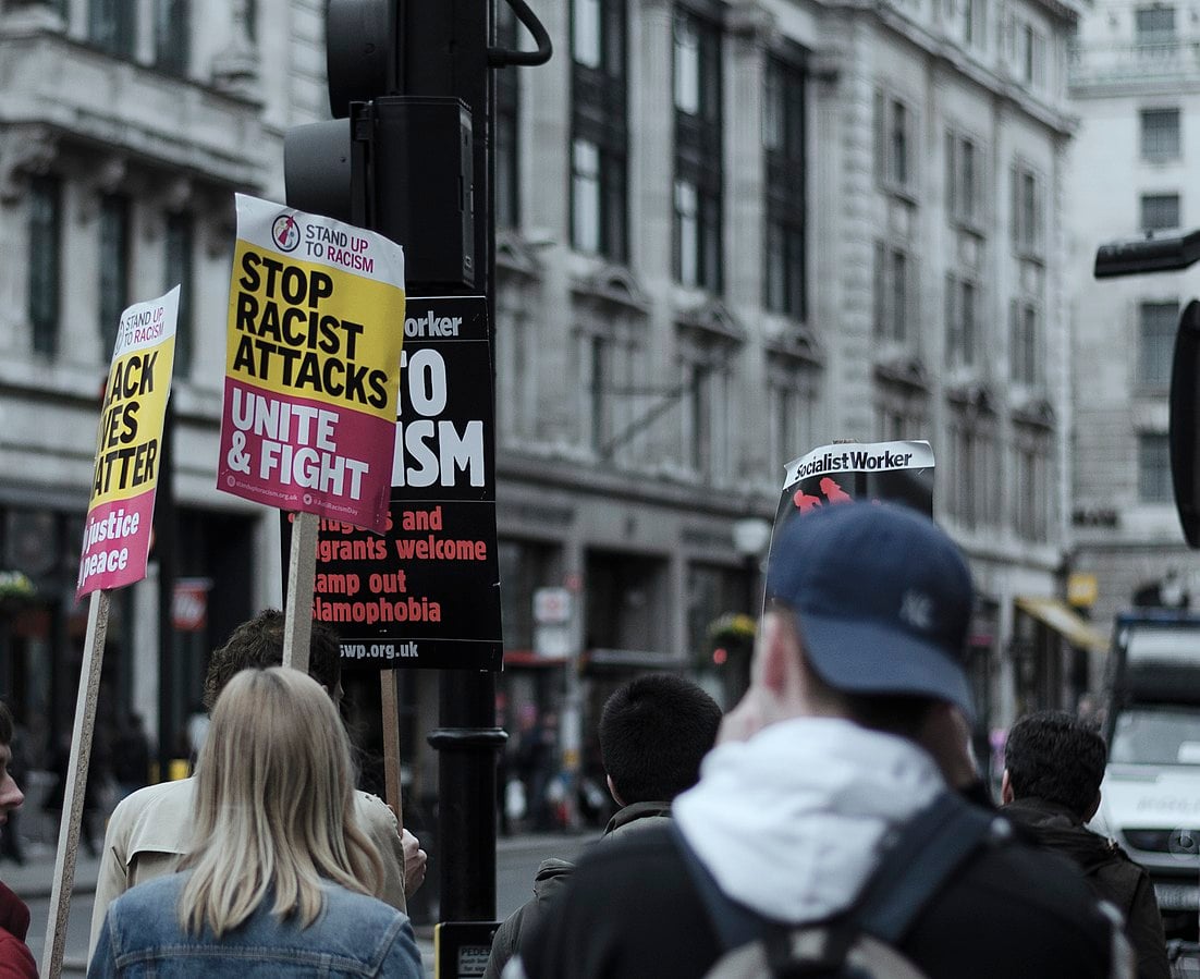 Anti-racism protestors in London stand holding 'say no to racism' signs.