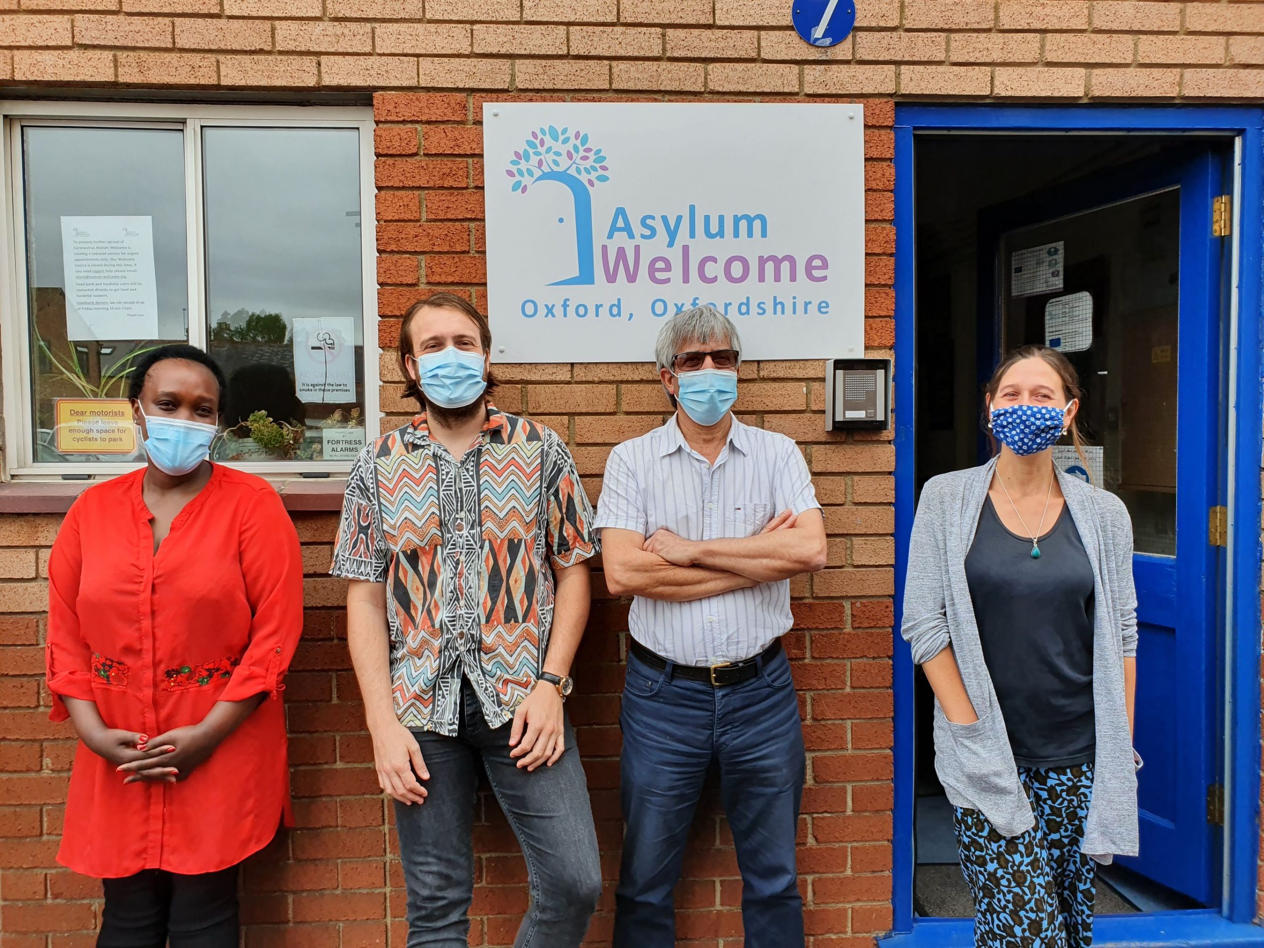 Four adults wearing masks in front of Asylum Welcome. From left to right: Caritas Umulisa, Simon Dawson, Almas Farzi ('Navid'), Helena Cullen