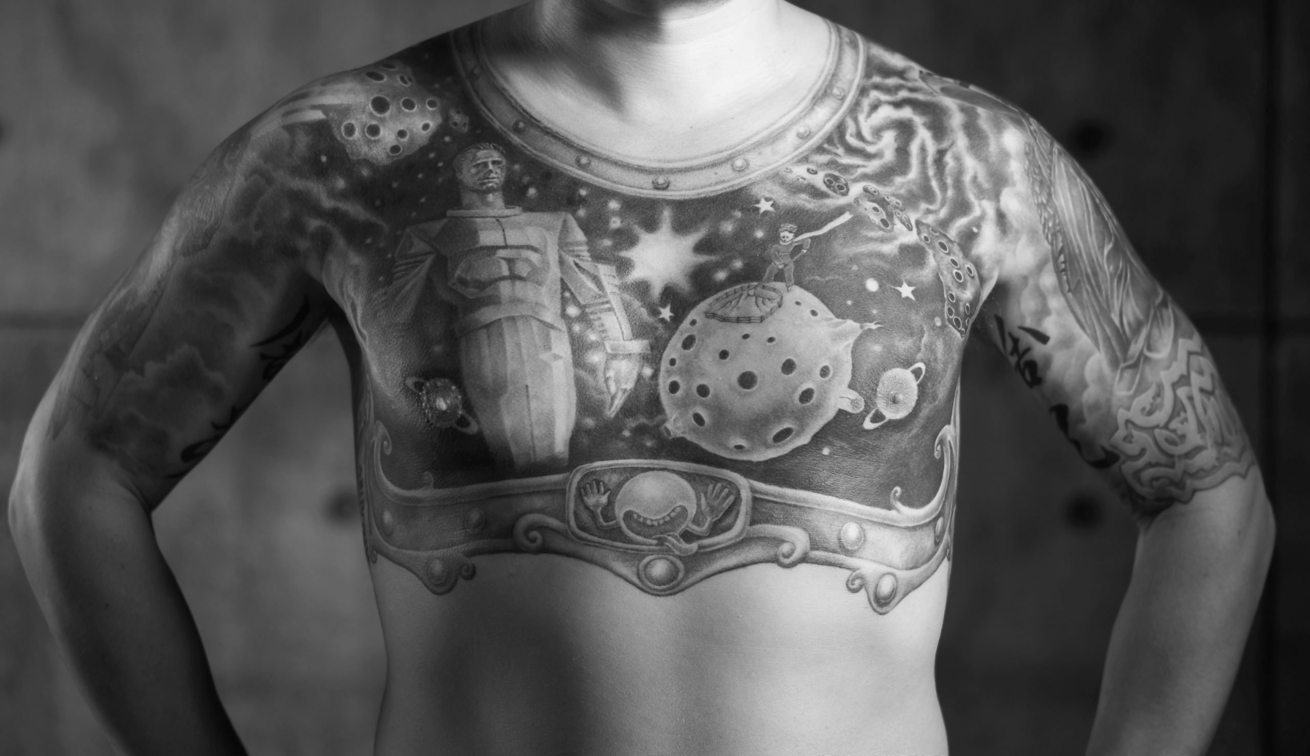 A black and white image of a man's chest featuring a large tattoo. 