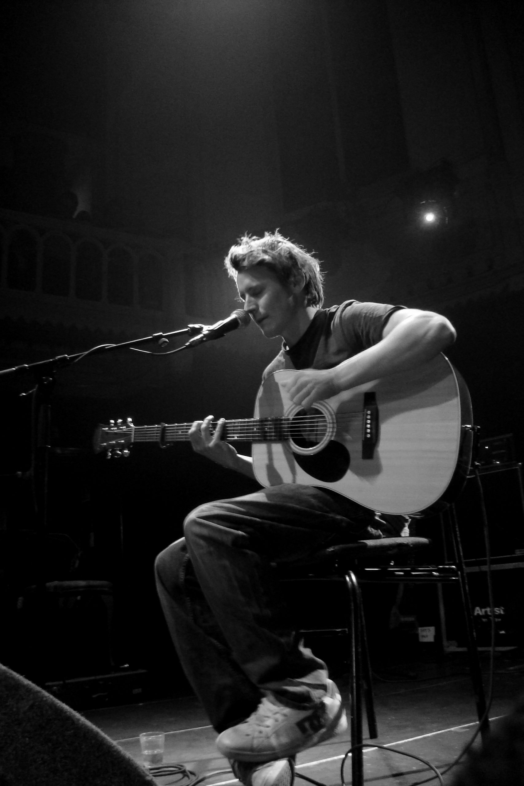 Ben Howard performing at Paradiso, Amsterdam, singing and playing the acoustic guitar whilst seated.