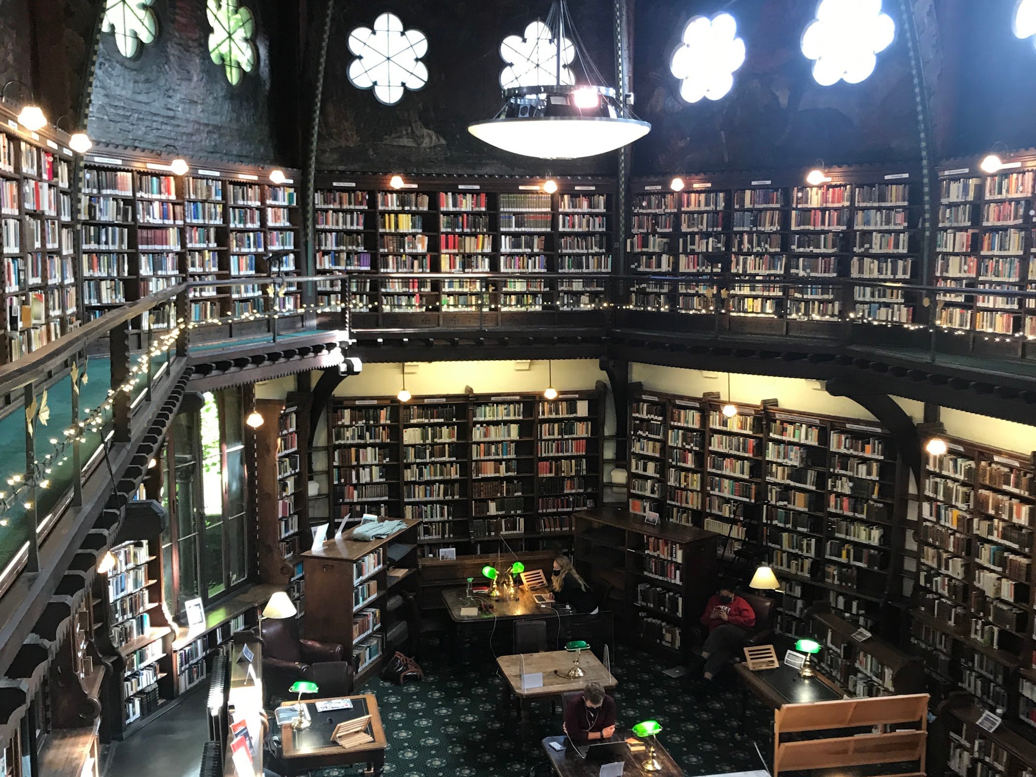 A photo taken from the top floor of the Oxford Union Library showing bookshelves and people working on the bottom floor. 