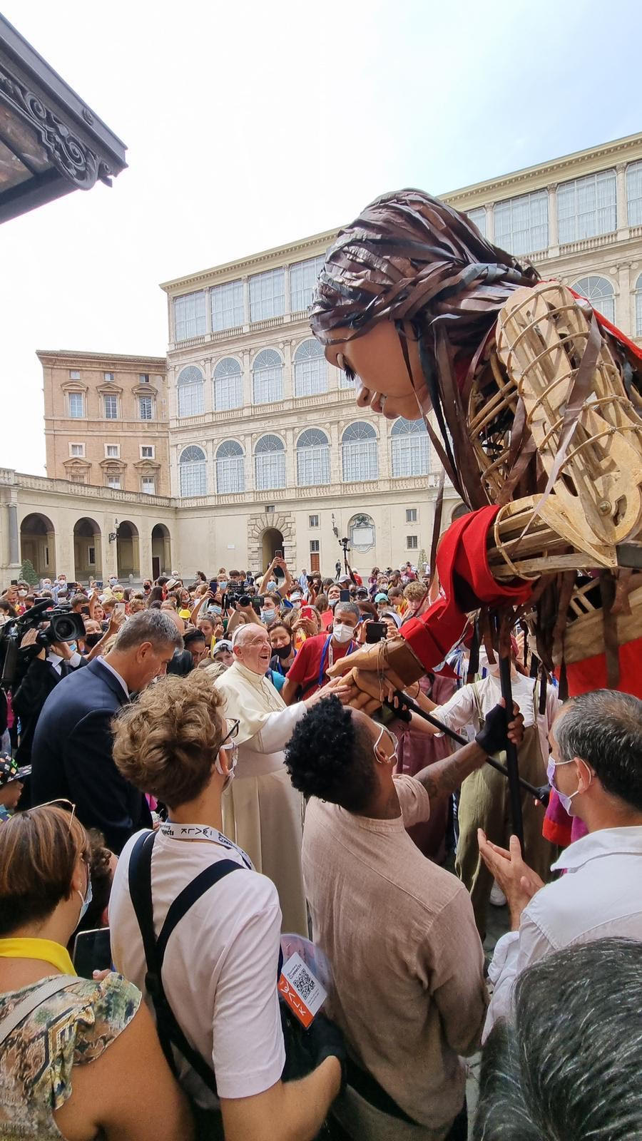 A large puppet of a young girl reaches down to shake the hand of Pope Francis.