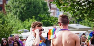 Image of two men at a Pride parade, one of whom is holding the LGBTQ+ pride flag.