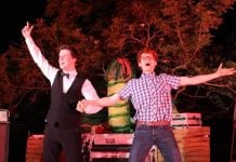 two men sing onstage in front of a giant plant