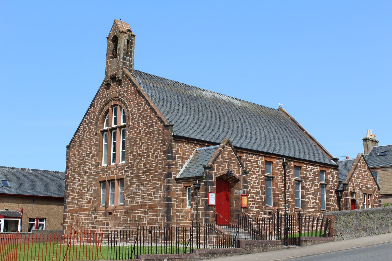 A picture of a small brick church with a red door against a blue sky