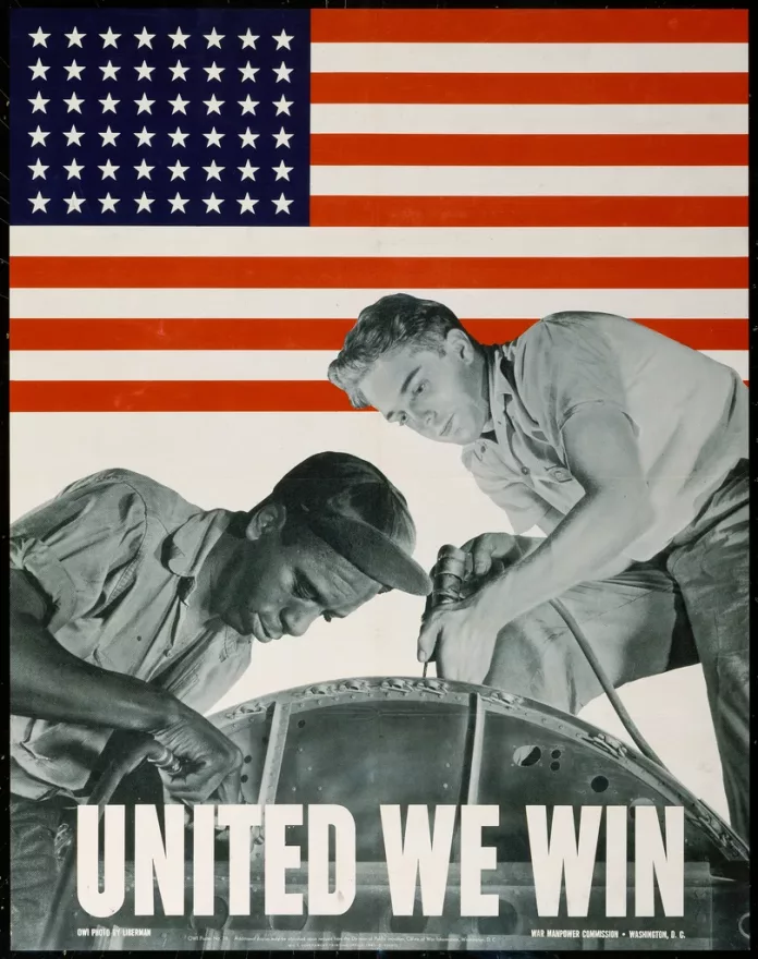 alt= A black man and a white man repair a machine together with the text 'United We Win' over the front. The background is a US flag.