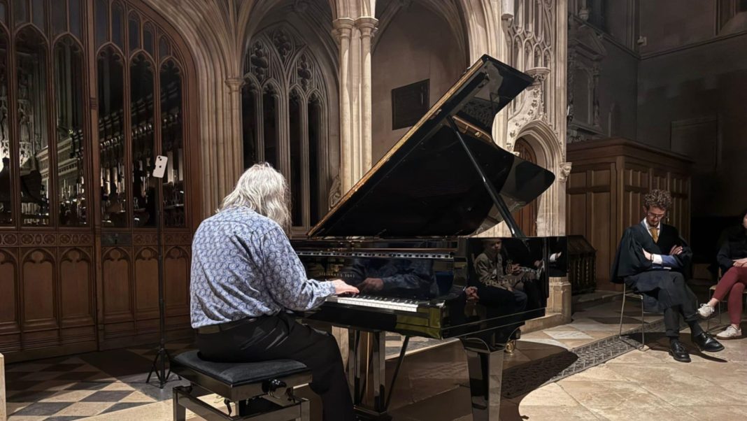 Lubomyr Melnyk sits at a grand piano, back to the camera, hunched over it as he plays his Continuous Music